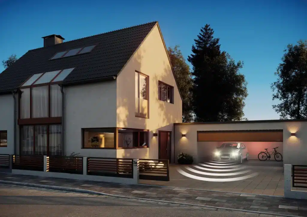 Modernes Haus mit beleuchteter Garage, einem darin geparkten Auto und Fahrrädern in der Nähe. Abendstimmung mit Bäumen im Hintergrund.