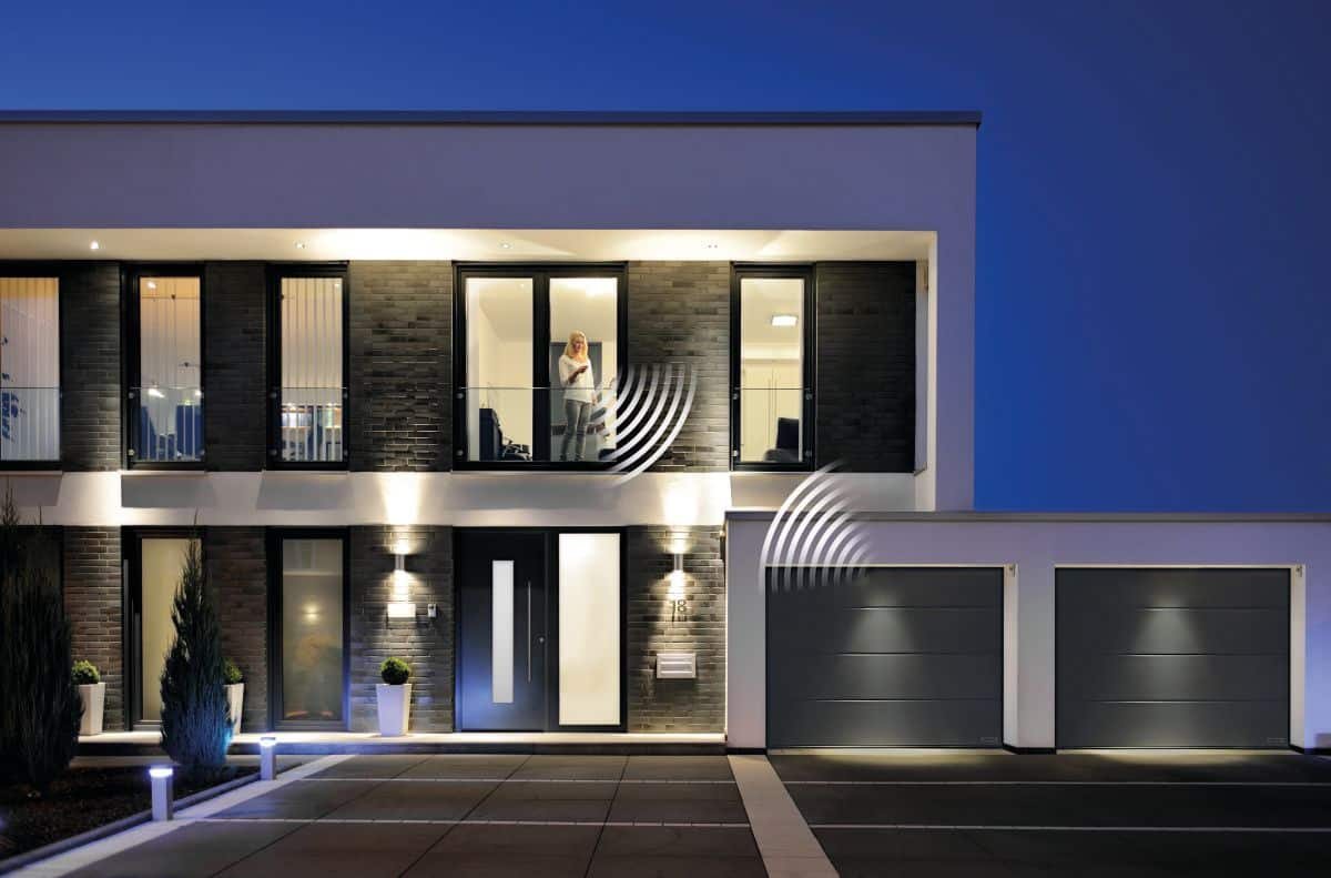 Garagentor mit Handy öffnen: modernes Haus in der Dämmerung mit beleuchteter Garage.