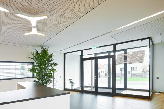 Moderne Bürolobby mit großen Glastüren, Zimmerpflanzen, eleganten Theken und einzigartiger Deckenbeleuchtung.